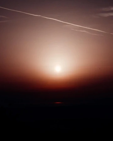 Sunset over a dark horizon with a visible contrail. The light creates a warm glow and highlights the atmospheric perspective.