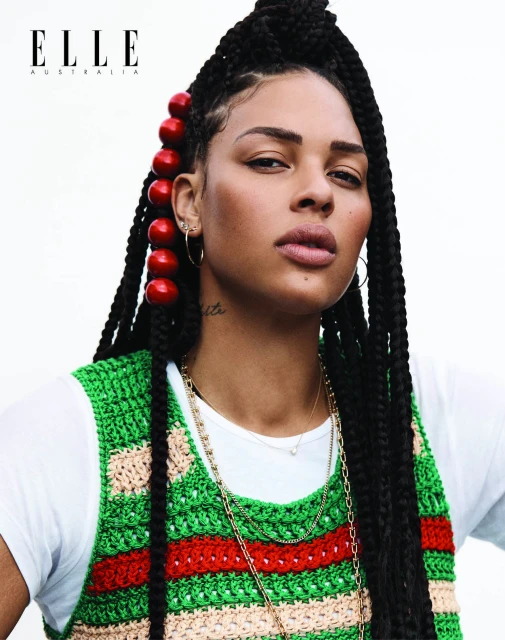 Portrait of an African American woman with braided hair, red beads, and a crocheted vest against a bright background. Elle Australia logo visible.