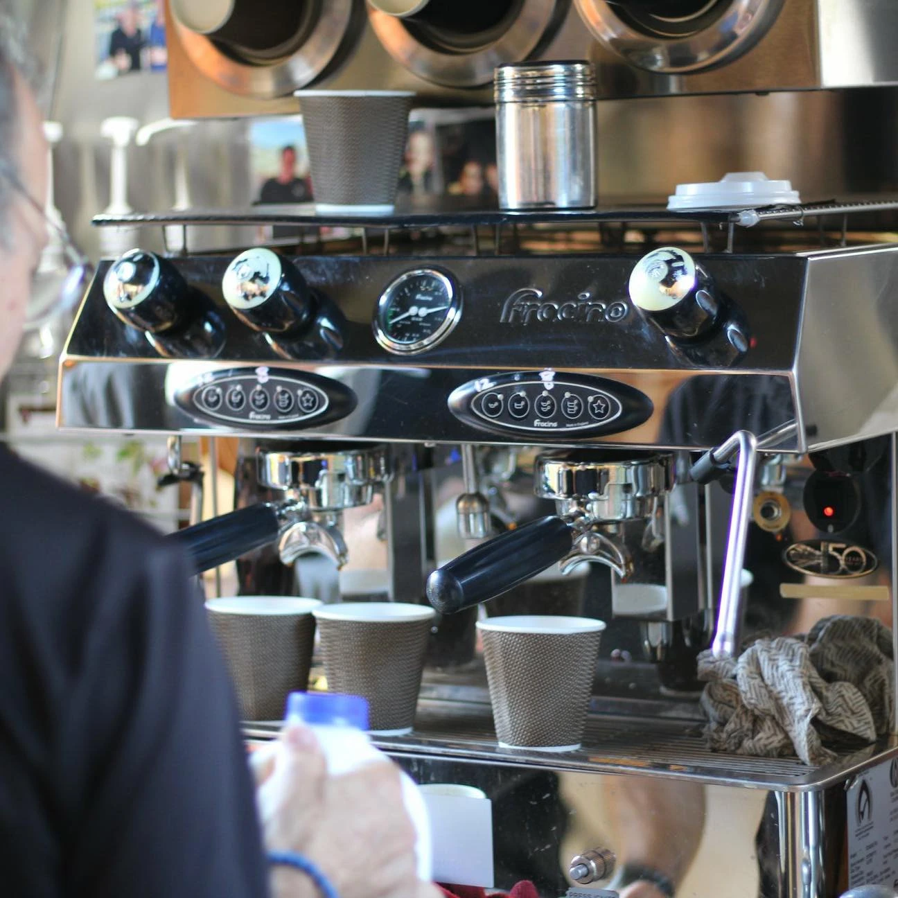 Commercial espresso machine in a coffee van with paper cups and a person holding a milk bottle in the foreground