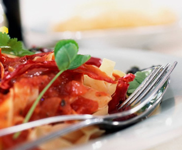Overhead shot of pasta dish topped with red sauce, parsley, and a sprig of clover, served on a white plate with a fork.