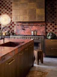 Luxury kitchen interior featuring red marble countertops, checkered tiled walls, wooden cabinets, and a metal range hood.