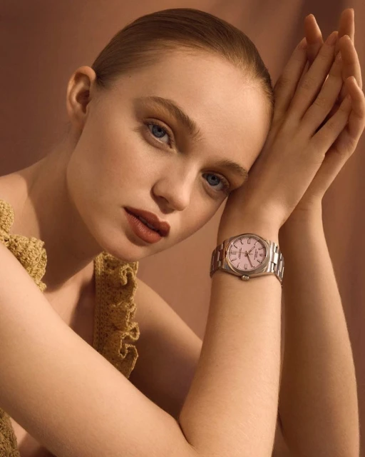 Elegant studio shot of a young woman wearing a watch with a silver band, with her hands near her face and a soft, neutral backdrop.