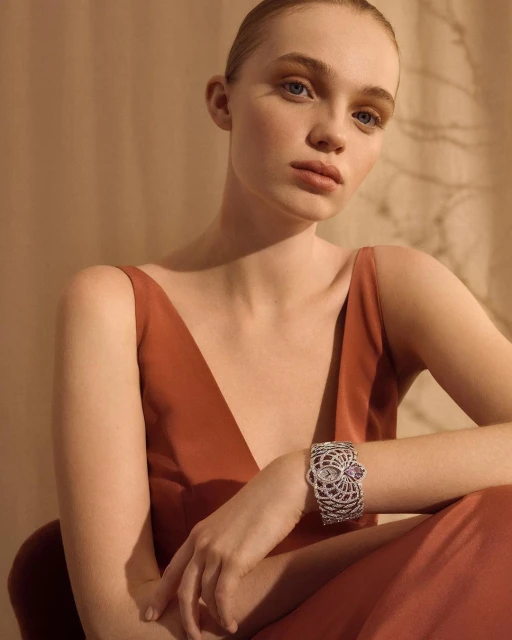 Elegant woman with updo poses indoors wearing a rust-colored dress and a vintage-inspired silver bracelet with filigree details.