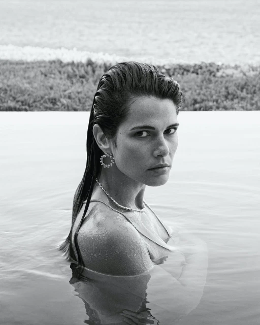 Monochrome portrait of an adult woman in water, wearing jewelry; a tranquil outdoor scene with a natural background and a soft, desaturated palette.