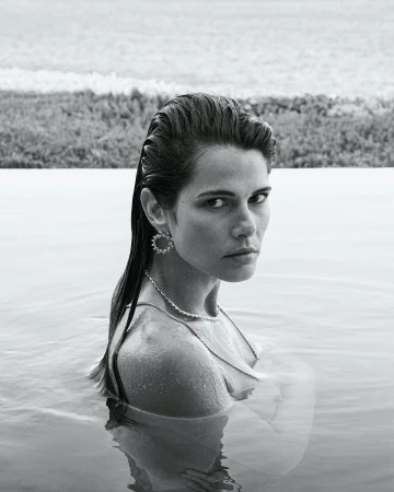 Monochrome portrait of an adult woman in water, wearing jewelry; a tranquil outdoor scene with a natural background and a soft, desaturated palette.