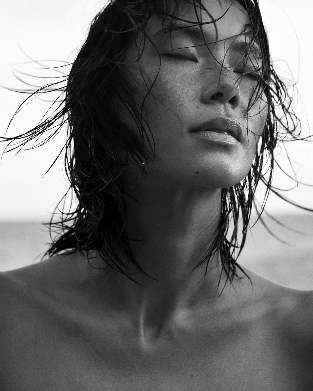 Close-up portrait of a woman with wet hair and eyes closed against an outdoor sky background
