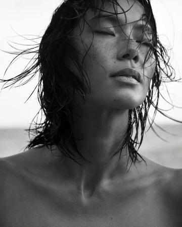 Close-up portrait of a woman with wet hair and eyes closed against an outdoor sky background