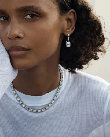 Close-up portrait of a woman wearing a diamond tennis necklace and matching drop earrings with a white ribbed top.