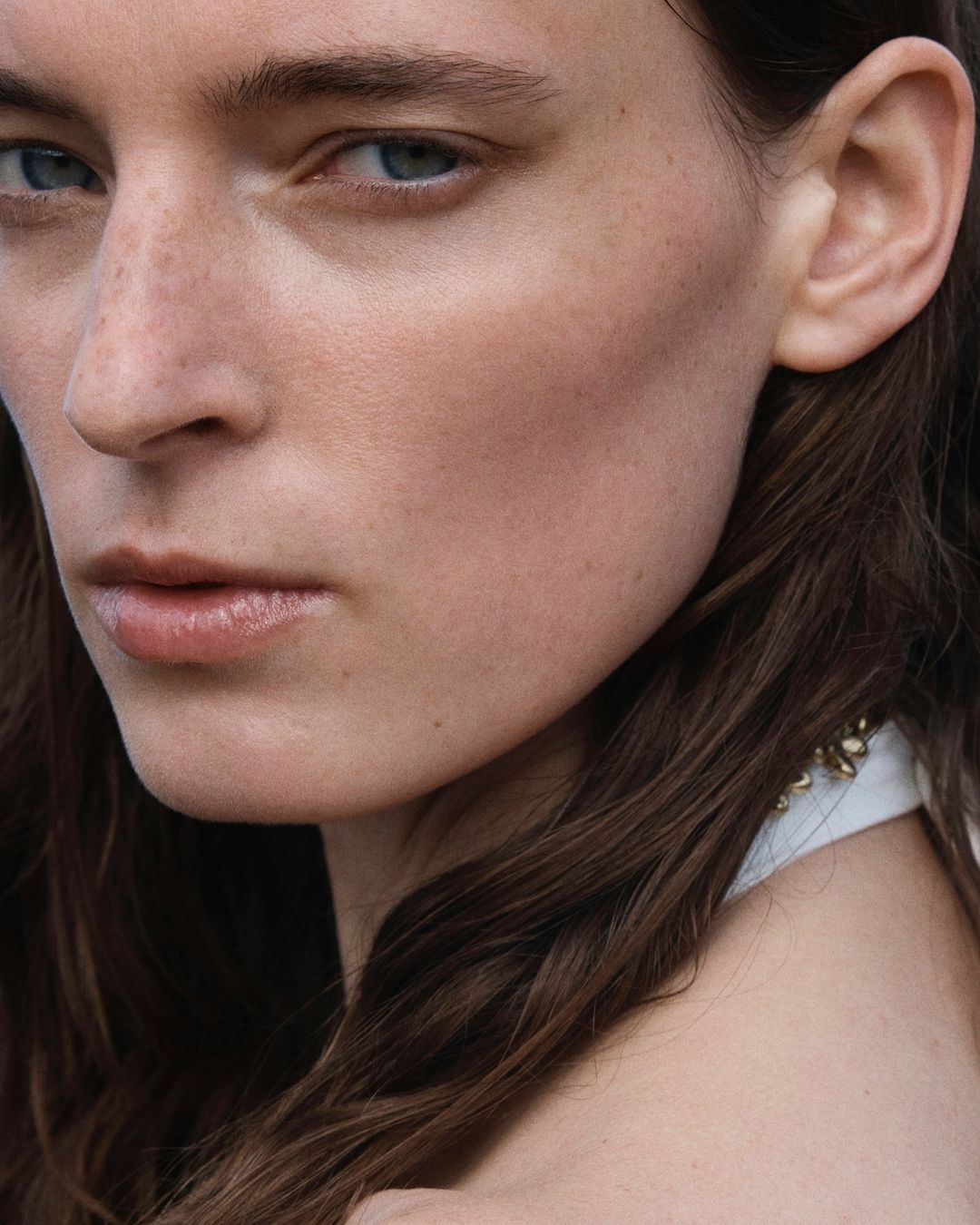 Close-up portrait of an adult female with fair skin and freckles, featuring brown hair and light blue eyes, captured in natural lighting.