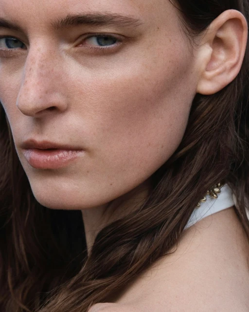 Close-up portrait of an adult female with fair skin and freckles, featuring brown hair and light blue eyes, captured in natural lighting.