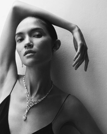 Close-up monochrome portrait of a woman wearing a diamond necklace and earrings with her arm raised