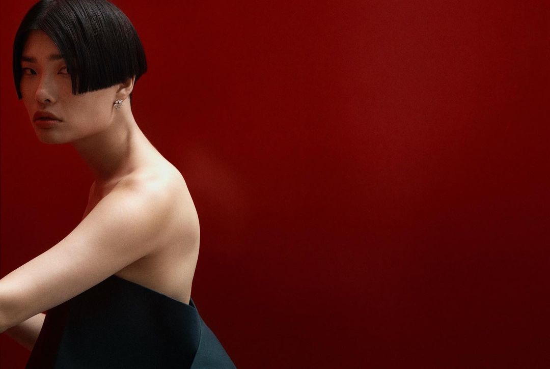 Portrait of an adult female with black bob hairstyle wearing a dark dress against a solid red background in a photo studio.