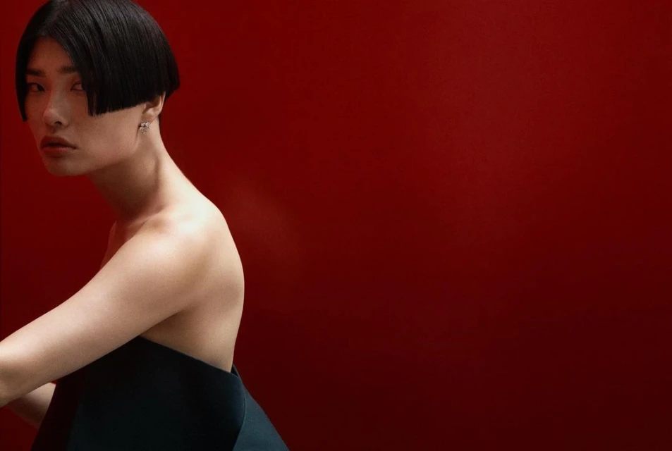Portrait of an adult female with black bob hairstyle wearing a dark dress against a solid red background in a photo studio.