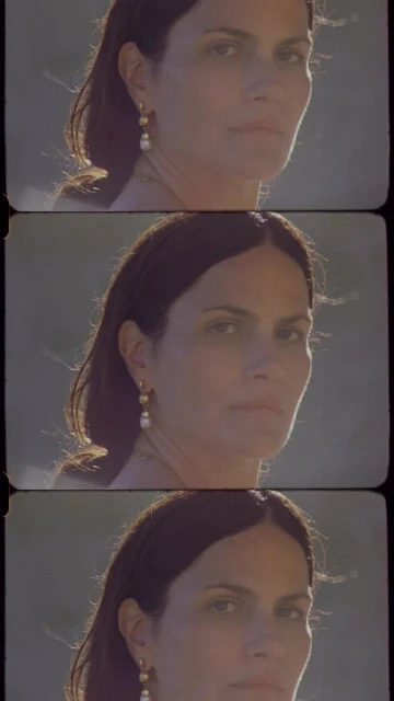 Portrait of a woman with dark hair and pearl earrings, lit by natural light, wearing a simple top, in a triple exposure effect.