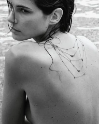 Close-up monochrome portrait of a woman with wet hair and a delicate layered silver body chain resting on her bare back, photographed by Amie Milne.