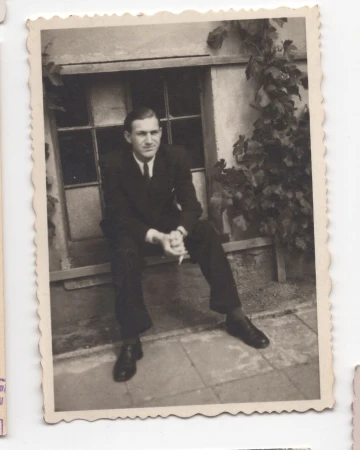Vintage monochrome photograph of a seated man in a dark suit against an exterior wall with climbing ivy.