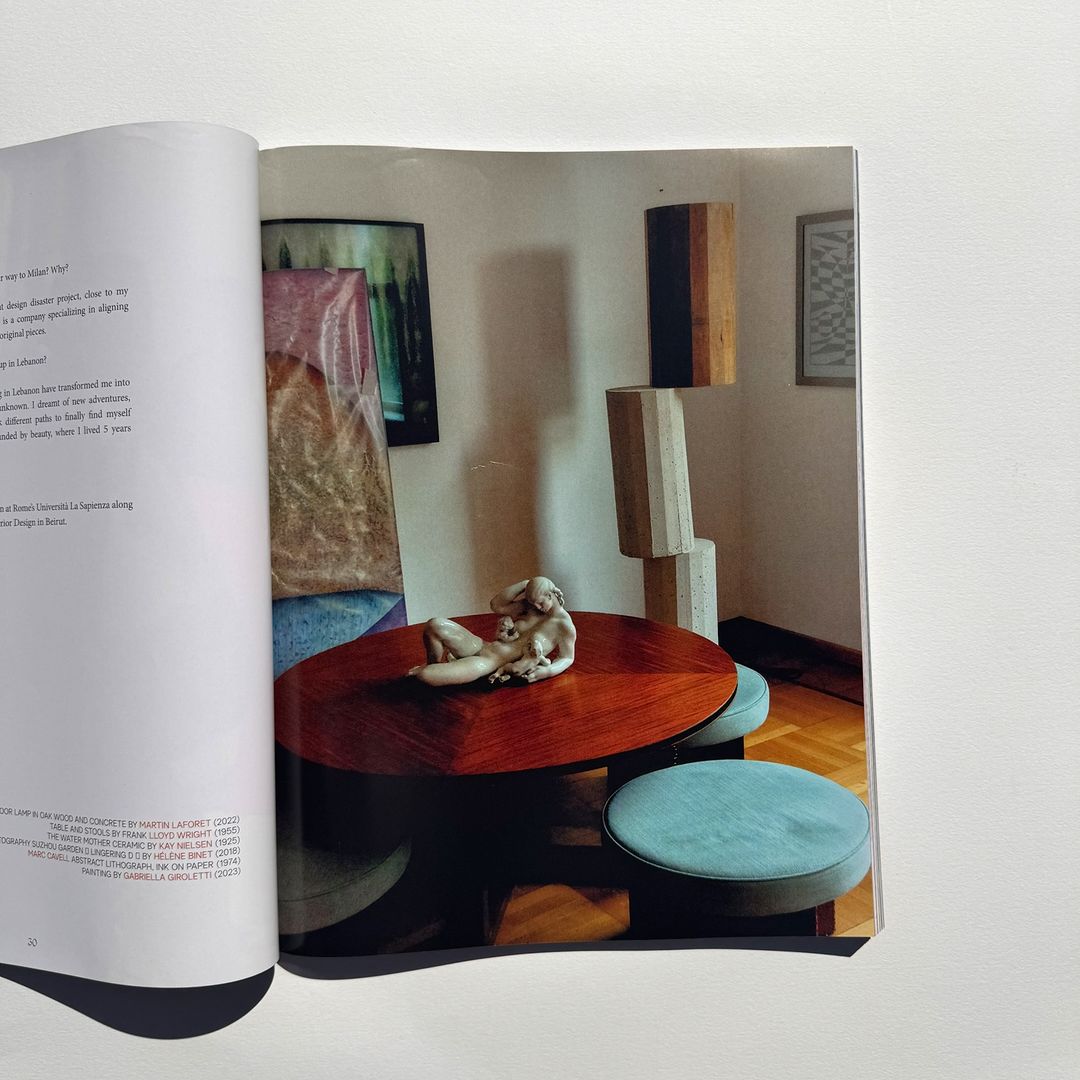 Magazine spread featuring a photo of a coffee table with a sculpture, surrounded by stools and abstract art in the background.