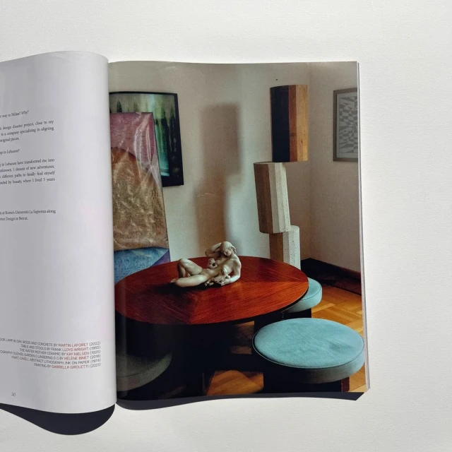 Magazine spread featuring a photo of a coffee table with a sculpture, surrounded by stools and abstract art in the background.