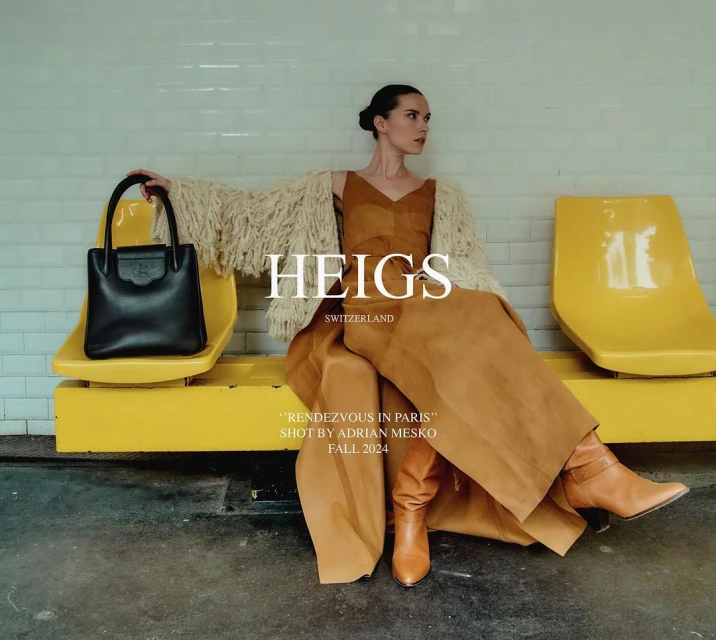 Fashion shot in subway: woman poses in caramel jumpsuit, tan boots, and fuzzy sweater, seated and holding a black leather handbag.