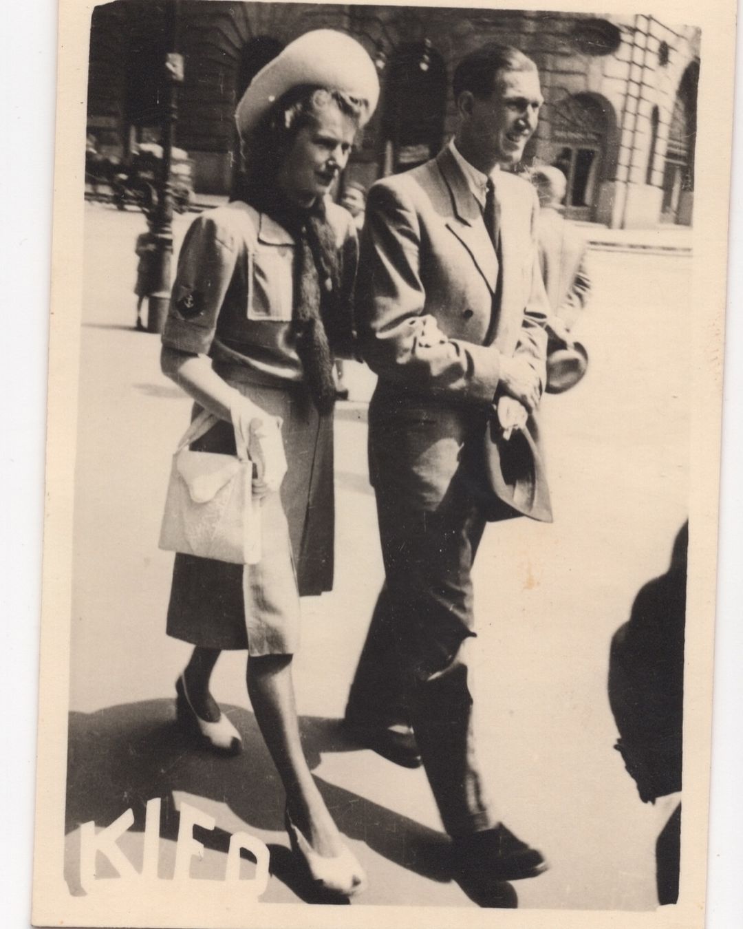 Black and white photograph of a man and a woman walking arm in arm on a city street, photographed by Adrian Mesko.