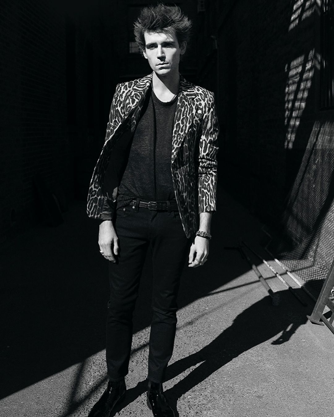 Man wearing a patterned animal print blazer and dark trousers standing outdoors in an alleyway by Adrian Mesko