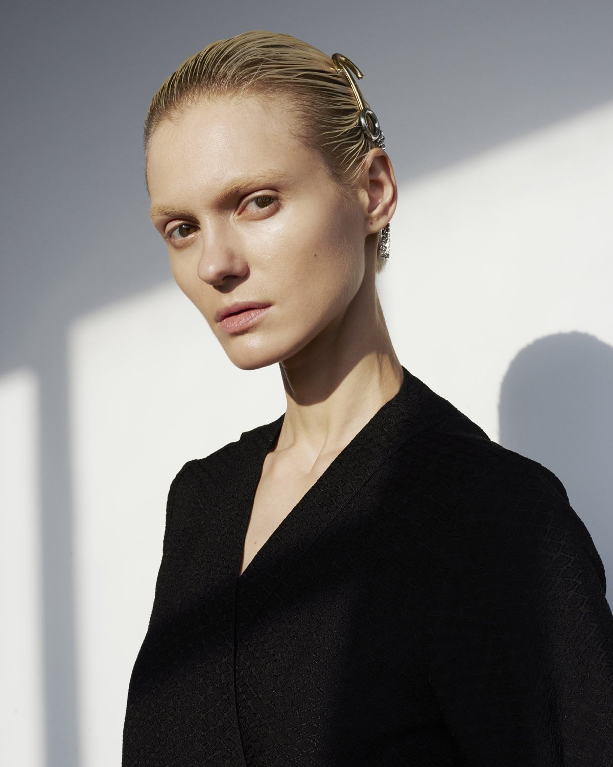 Close-up studio portrait of a fair-skinned adult female with wet, blonde hair and an ornate hair clip, wearing a black v-neck garment.