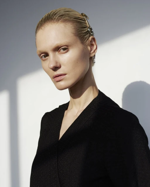 Close-up studio portrait of a fair-skinned adult female with wet, blonde hair and an ornate hair clip, wearing a black v-neck garment.