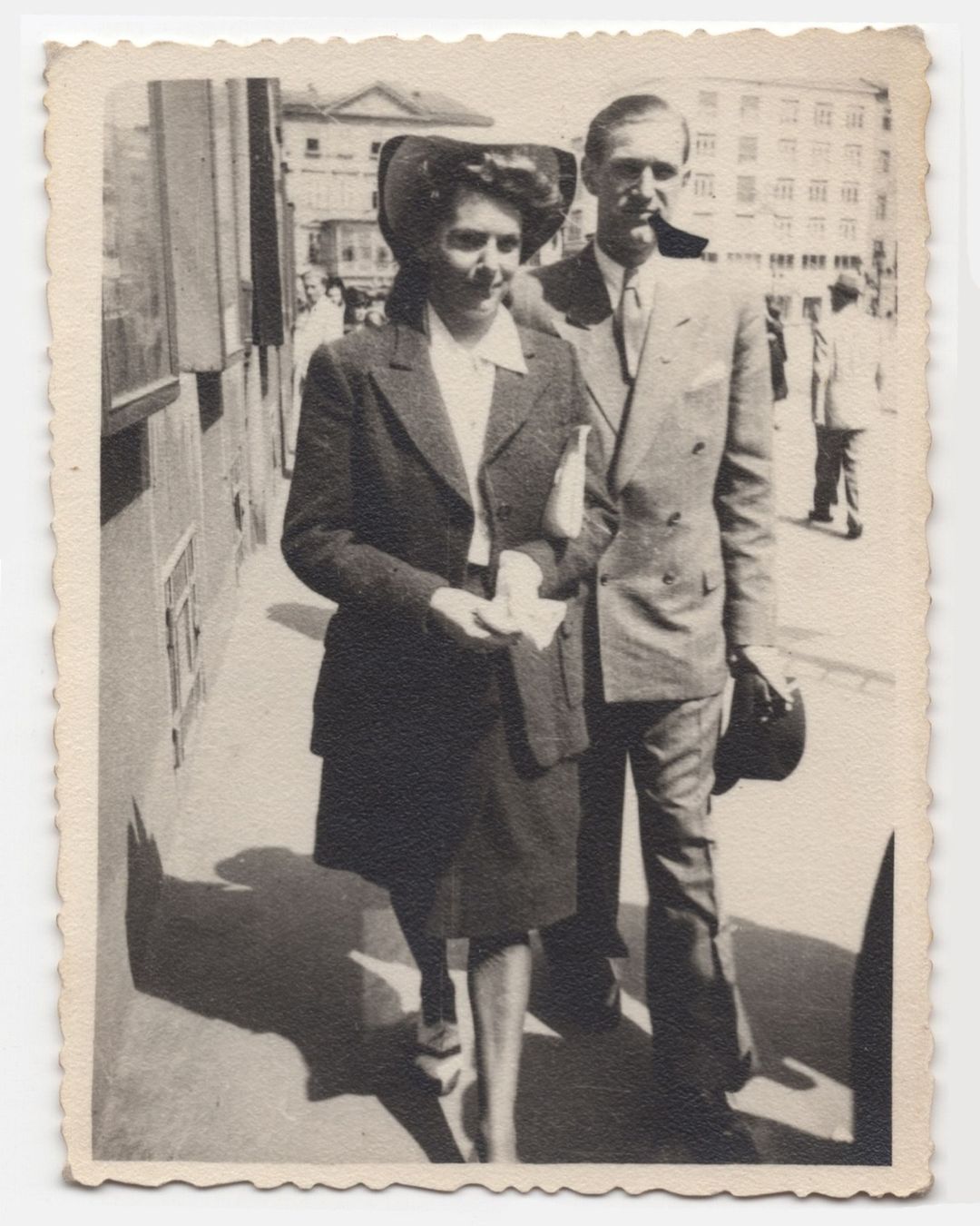 Vintage black and white photograph of a man and woman walking together down a sunlit city street.