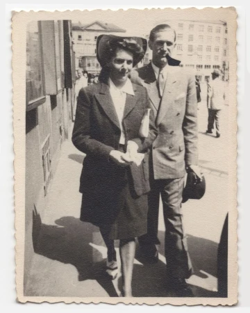 Vintage black and white photograph of a man and woman walking together down a sunlit city street.