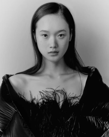 Monochrome portrait of an East Asian woman with long dark hair wearing a feathered top photographed by Adrian Mesko