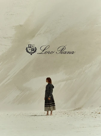 A woman in a patterned dress stands barefoot on pale sand against a towering chalk cliff, photographed by Adrian Mesko.