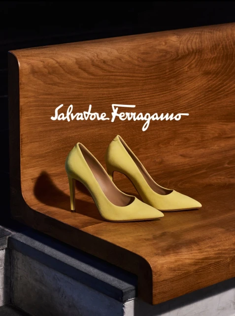 Pair of yellow high-heeled shoes showcased on a wooden surface with 'Salvatore Ferragamo' logo, against a dark, neutral background.