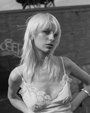 Portrait of a blonde woman wearing a lace-trimmed slip top outdoors against a brick wall with graffiti in Sydney.
