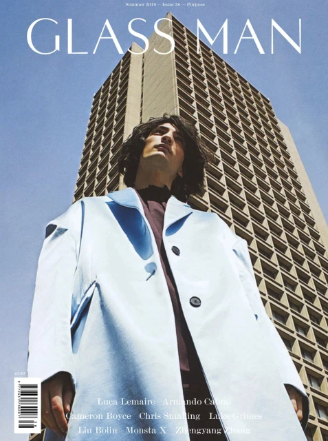 Magazine cover featuring a model in a light blue jacket and the 'Glass Man' title, set against a backdrop of a tall building.