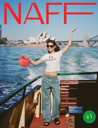 Woman on boat with Sydney Opera House and Harbour Bridge in background. She wears a white top, jeans, and holds a red purse.
