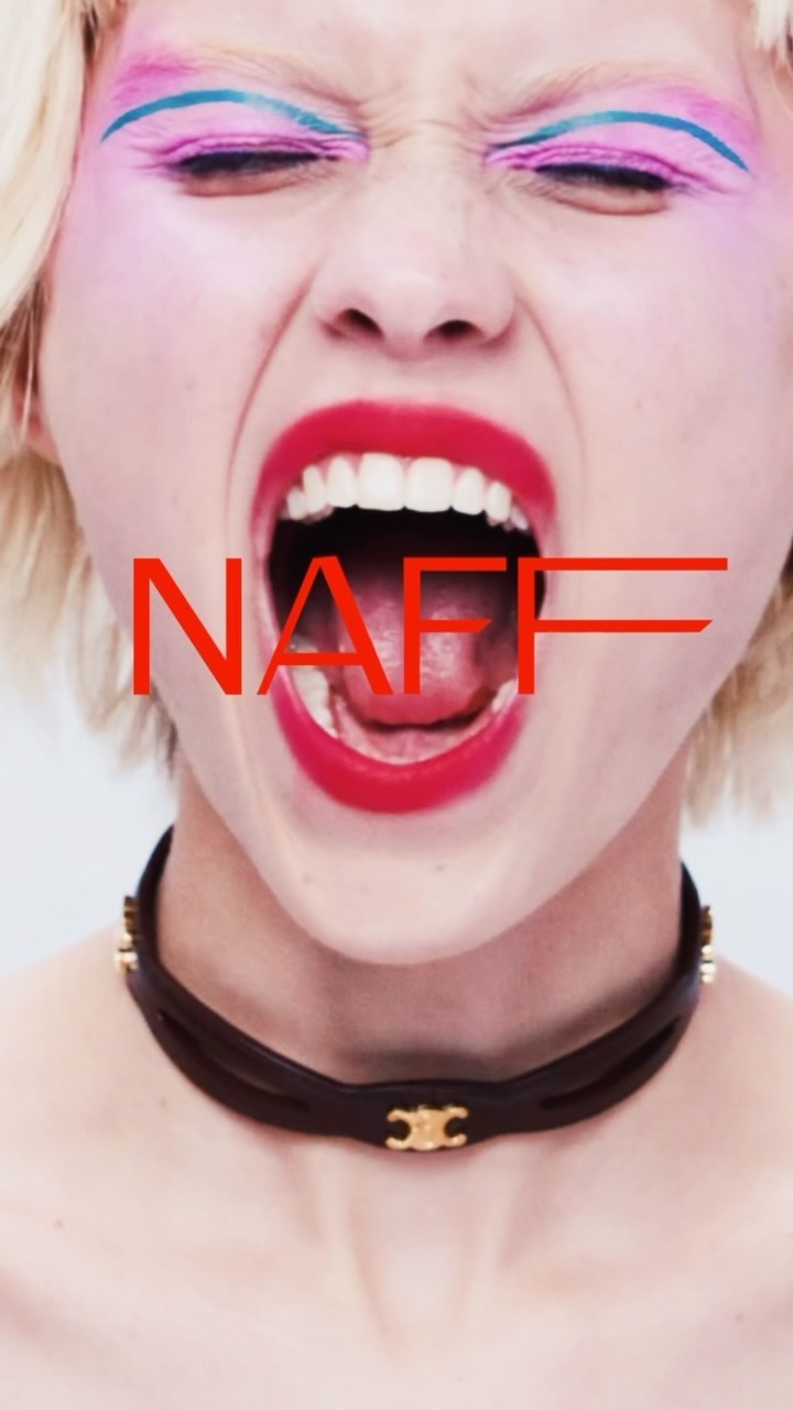 Close-up portrait of a woman with vibrant pink eyeshadow, blue eyeliner, and bright red lipstick yelling with her mouth wide open, wearing a black leather choker.