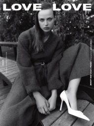 Black and white portrait of a woman seated on a wooden bench outdoors wearing a dark sweater and white high heels.