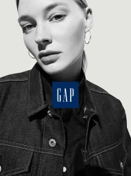Close-up black and white portrait of a woman wearing a dark denim jacket and hoop earrings against a light background.