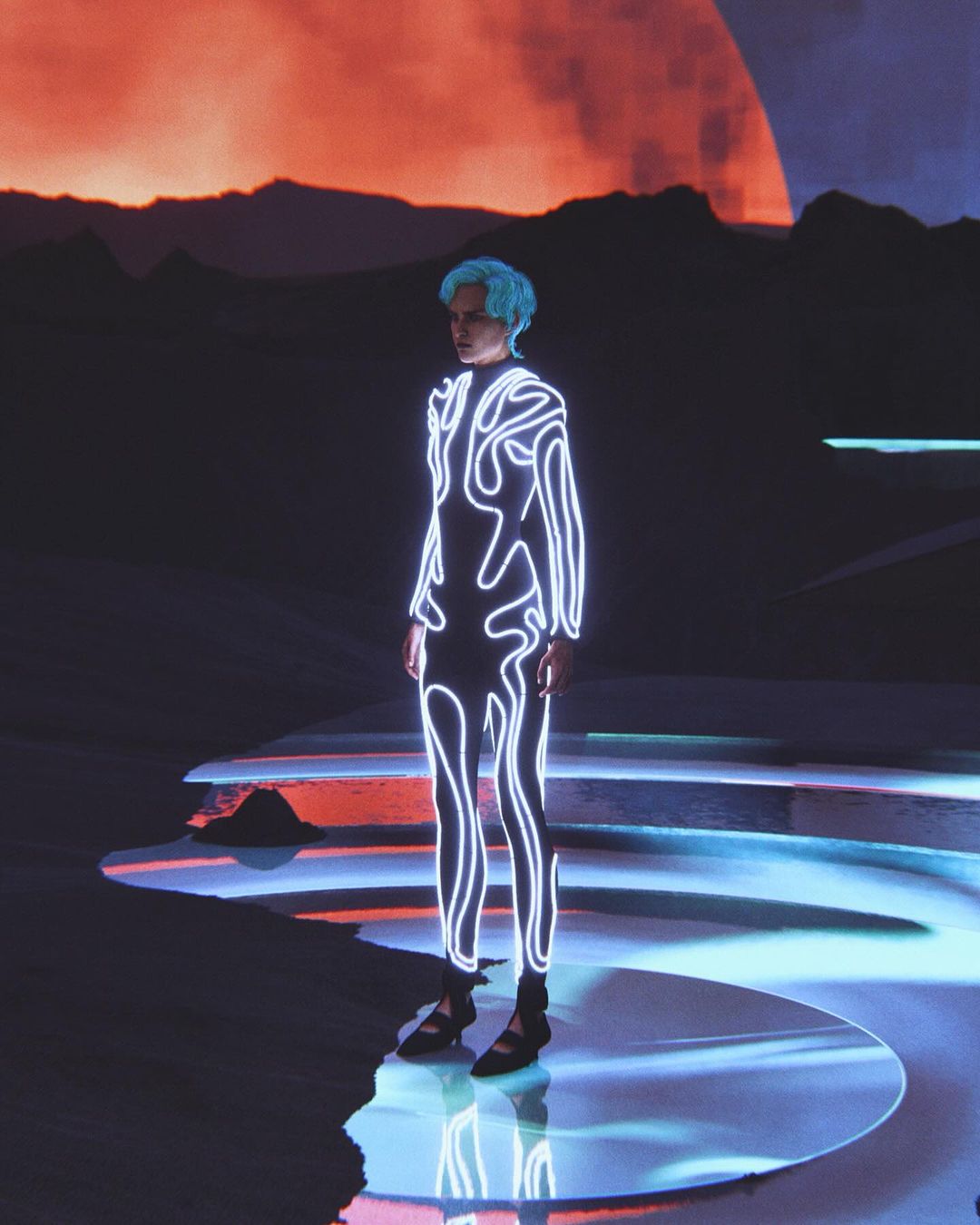 Person stands on illuminated stage in futuristic jumpsuit with blue hair, against a backdrop of a glowing planet and dark mountains.