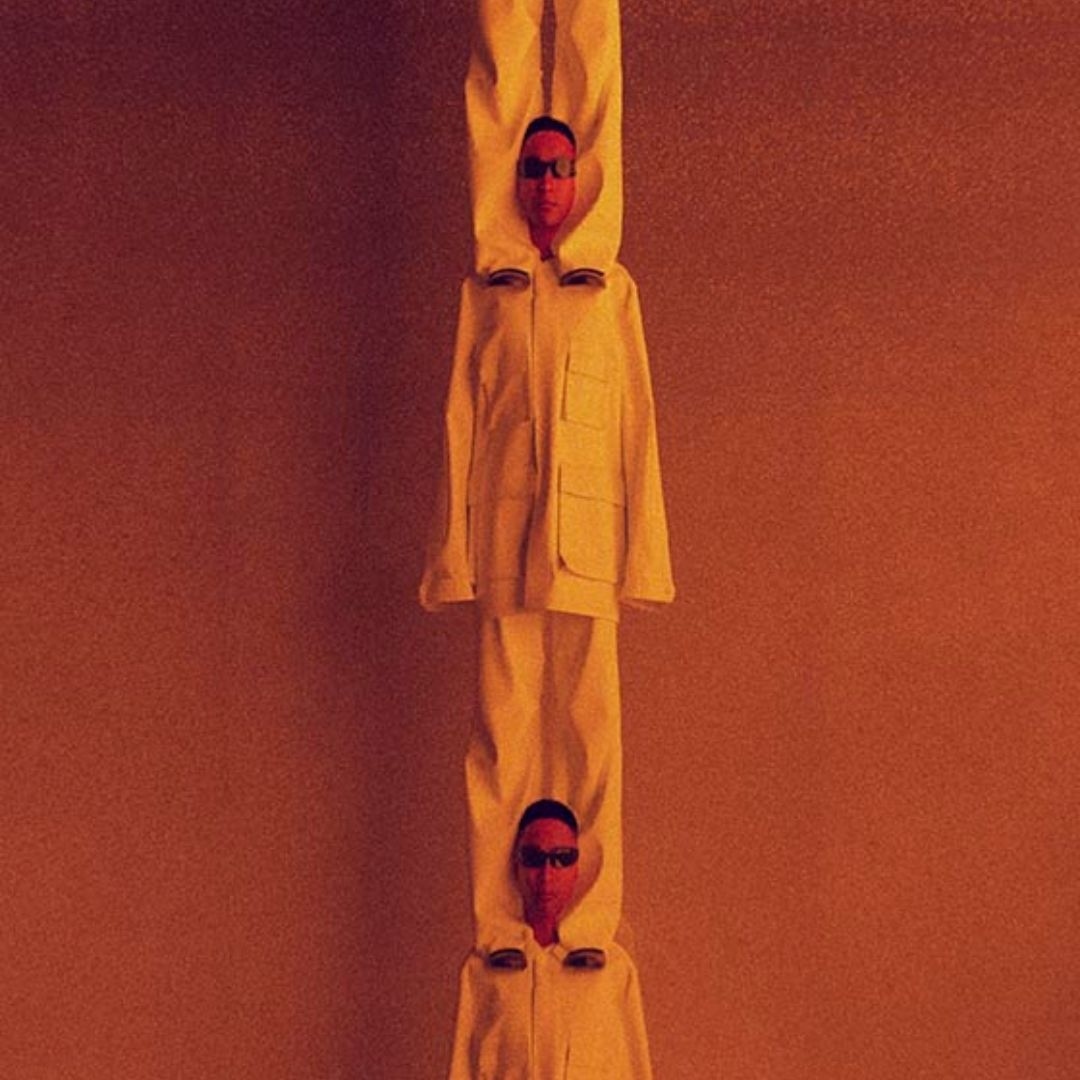 Two people stacked vertically, wearing matching off-white outfits and sunglasses against a monochromatic orange background. 