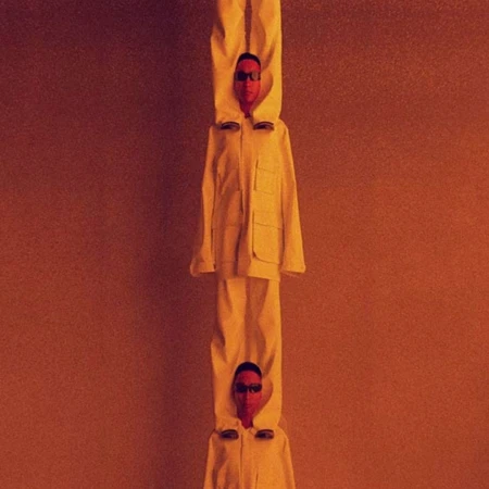 Two people stacked vertically, wearing matching off-white outfits and sunglasses against a monochromatic orange background. 