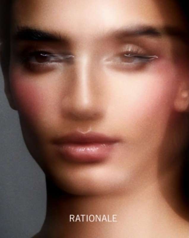 Close-up of a young adult female face with diffused lighting, pink blush, and soft focus in a beauty or fashion context. Minimal makeup.