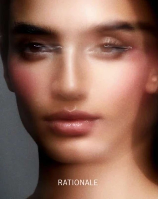 Close-up of a young adult female face with diffused lighting, pink blush, and soft focus in a beauty or fashion context. Minimal makeup.