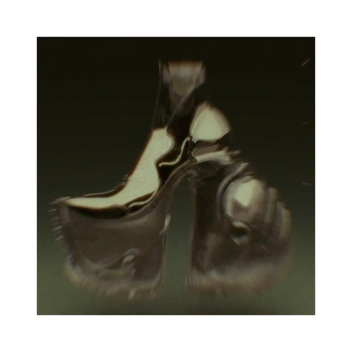 A high-heeled platform shoe is shown in a surreal style, likely fashion-related, with blurred focus against a dark, blurry backdrop.