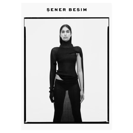Monochrome portrait of a model in a black ribbed turtleneck and sheer matching trousers against a white seamless backdrop.