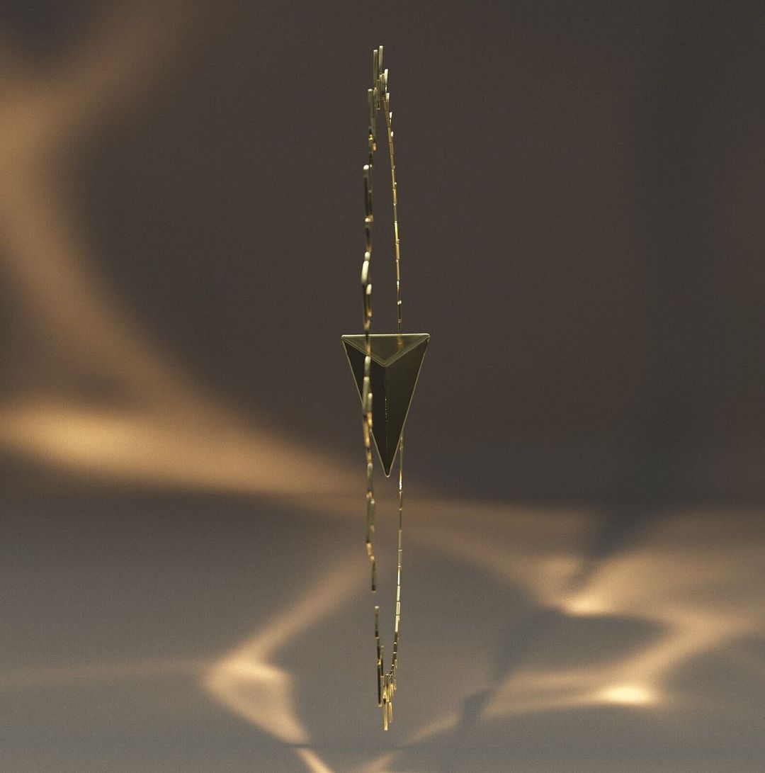 Abstract modern art: gold metal geometric mobile with triangle form and linear elements suspended against a blurred gradient background.