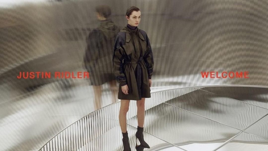 Woman in olive green coat dress and black heeled boots standing on a reflective grid surface with text overlay, fashion editorial.