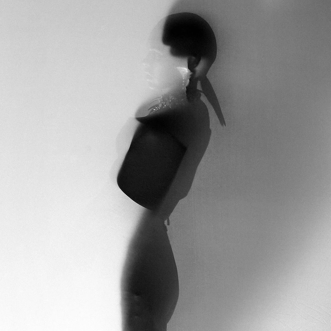 Monochrome photo of a blurred woman in profile against a white background holding a box, blending fashion with artistic expression.