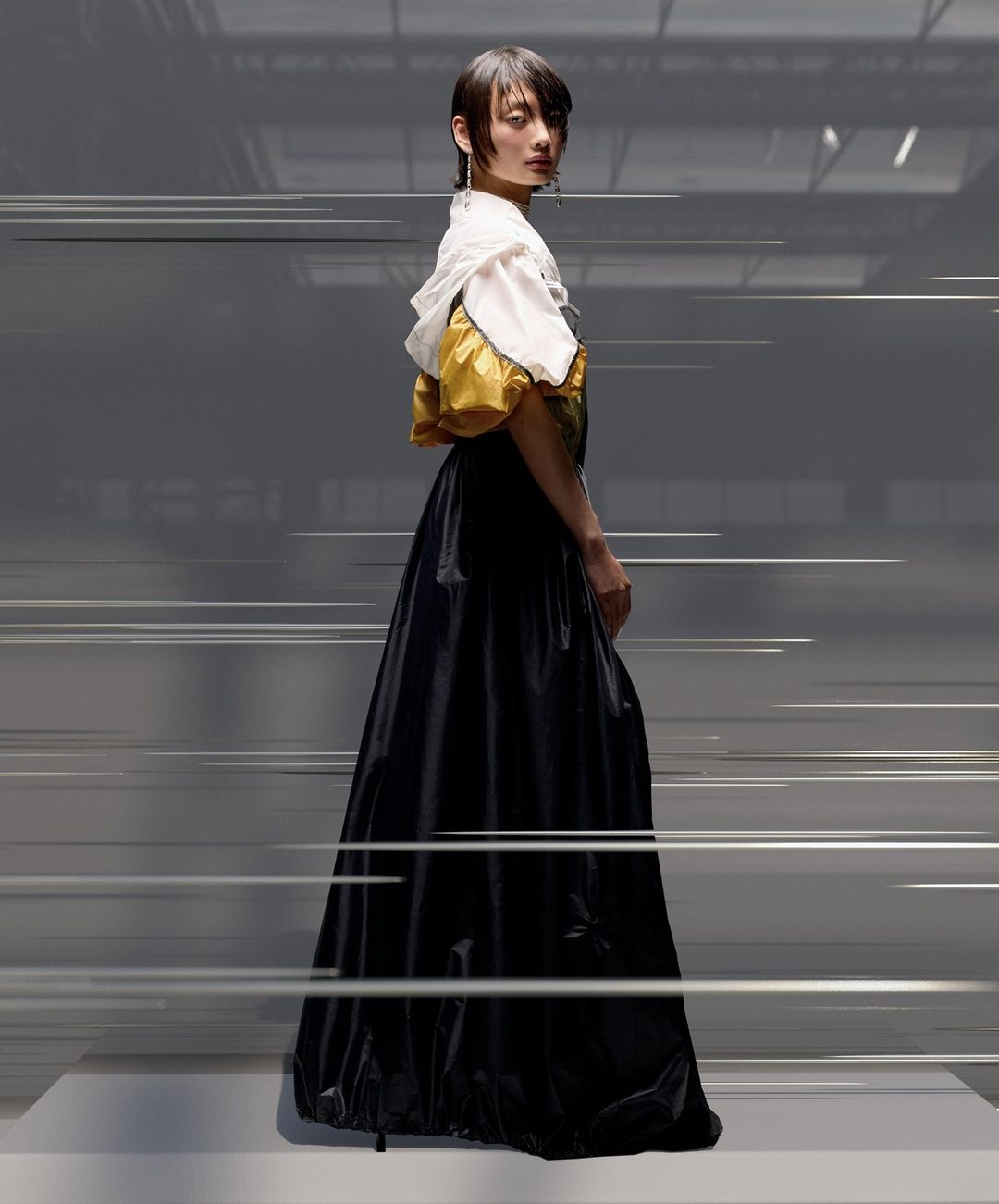 A woman poses in an oversized gown featuring a white bodice and black skirt in a studio environment, with motion-blurred lines creating a dynamic effect.