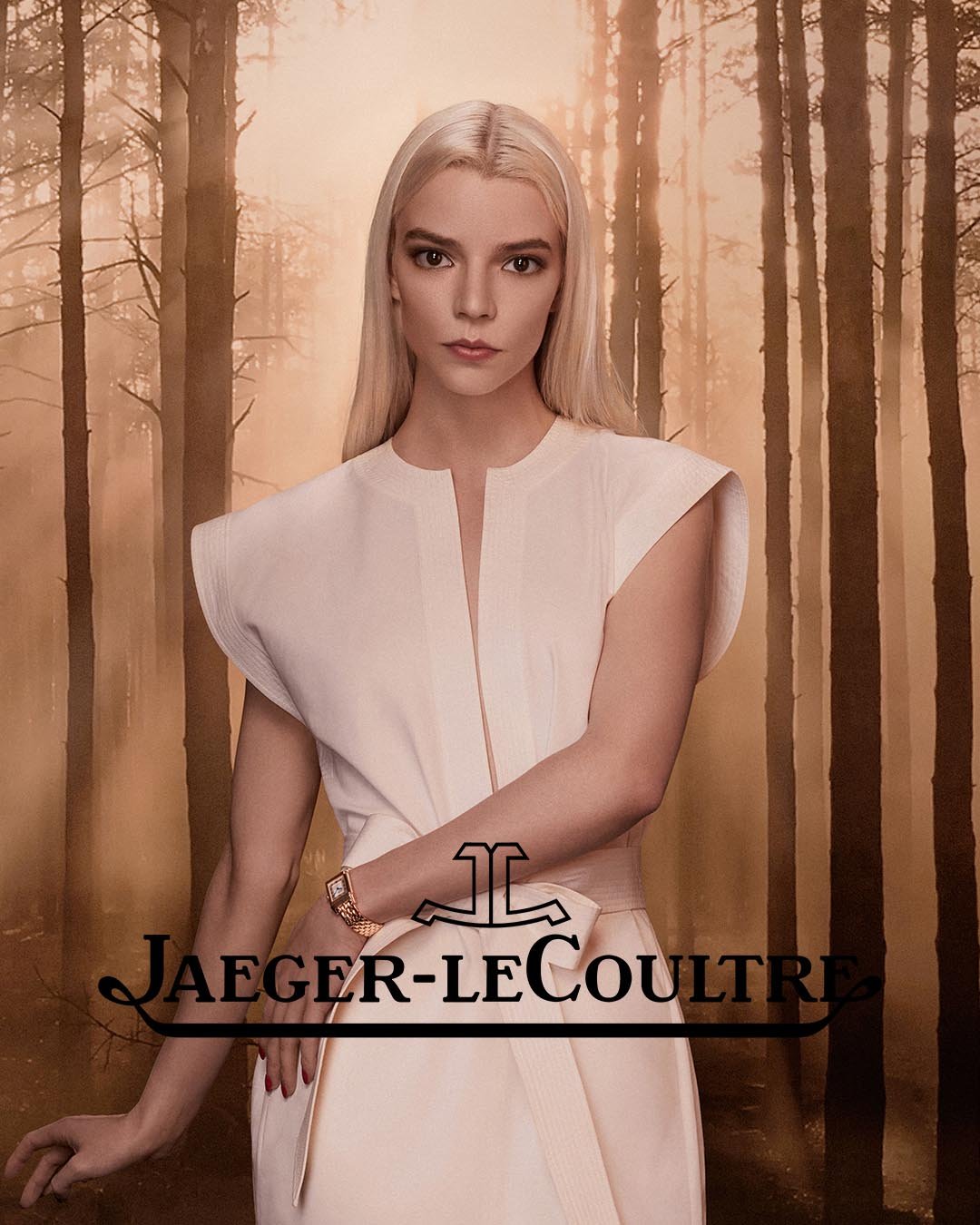 Anya Taylor-Joy poses in an elegant white dress and a gold watch with a forest background and a Jaeger-LeCoultre logo.